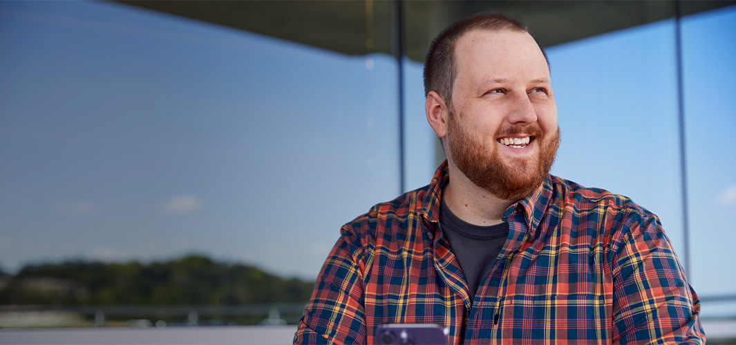 Topher, der sidder uden for en kontorbygning, smiler og kigger til siden.