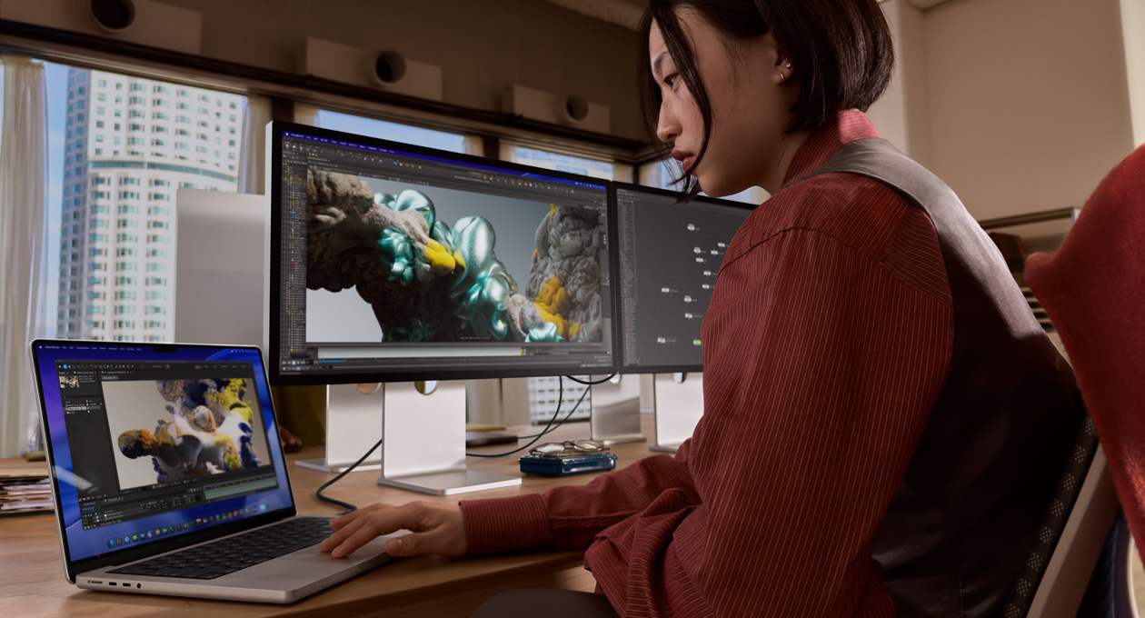 Persona biroja vidē strādā ar MacBook portatīvo datoru, kas ir savienots ar Studio Display XDR, izmantojot Thunderbolt 5 portu