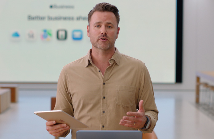 Apresentador a falar e a fazer referência a um iPad, um grande ecrã de apresentação mostra vários ícones de apps profissionais.