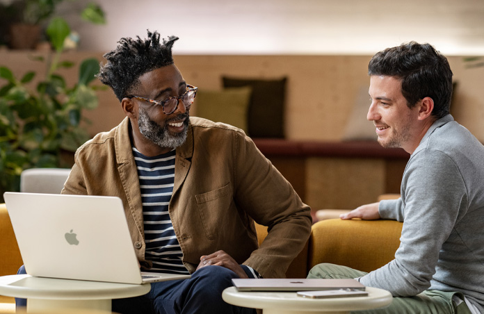 MacBook aberto sobre uma mesa, em frente a uma pessoa sorrindo