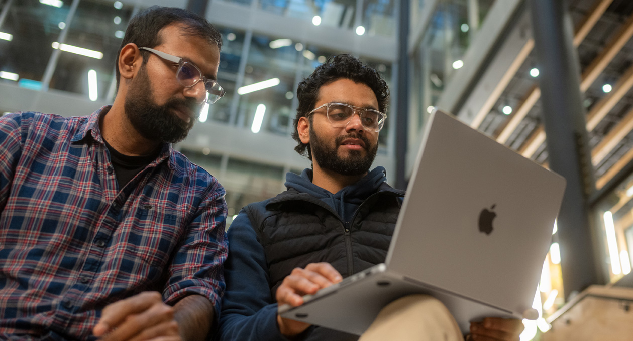 Two men in glasses looks at a MacBook Pro together