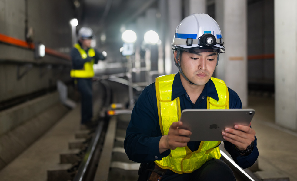 Một công nhân mặc áo và mũ bảo hộ nhìn vào iPad trong khi đang bảo trì đường hầm của Tokyo Metro.