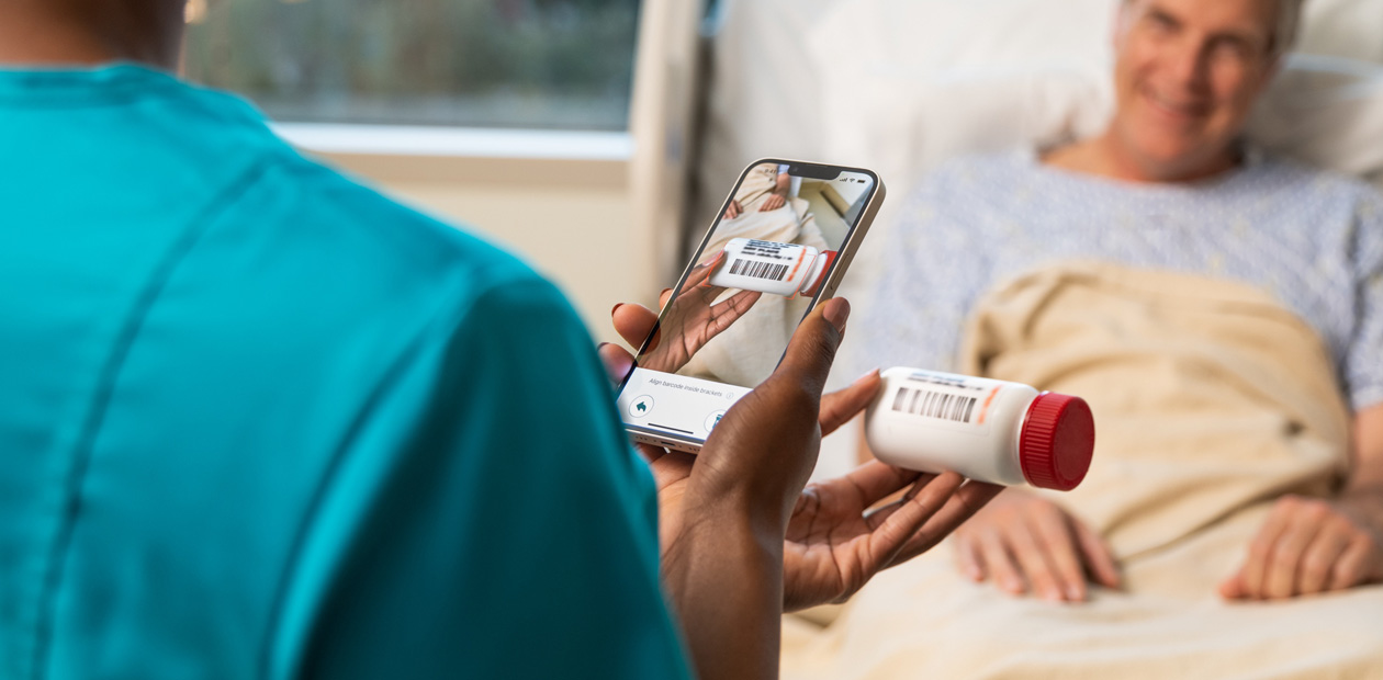 Une infirmière portant un uniforme turquoise balaye le médicament d’un patient avec son iPhone.
